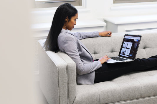 Professional woman working on a laptop while seated comfortably on a modern gray couch in a bright office setting.